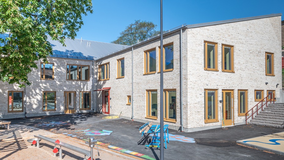 Förskola med ljus fasad och del av förskolegården med lekutrustning.
